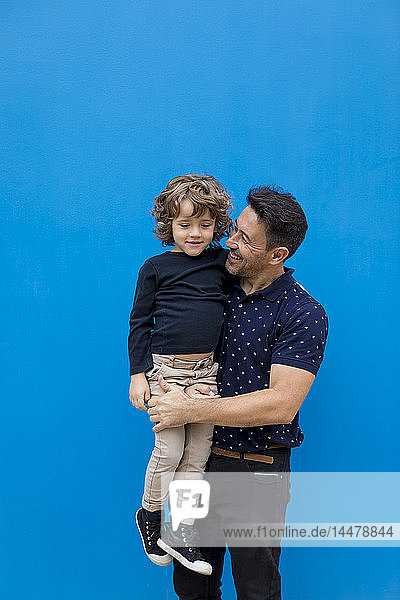 Glücklicher Vater trägt Sohn an blauer Wand