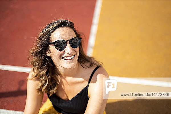 Porträt einer glücklichen Frau mit Sonnenbrille auf einem Sportplatz