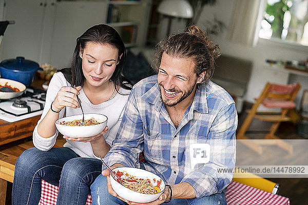Glückliches Paar sitzt am Küchentisch und isst Spaghetti