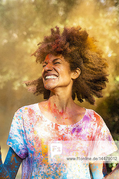 Frau schüttelt den Kopf  voll bunter Pulverfarbe  feiert Holi  Fest der Farben