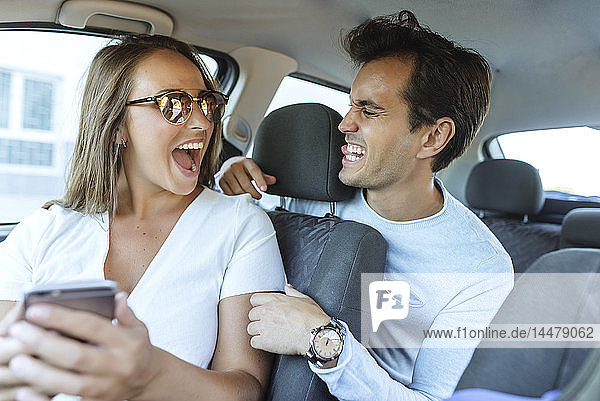 Happy couple in car grimacing with man on back seat and woman on front passenger seat
