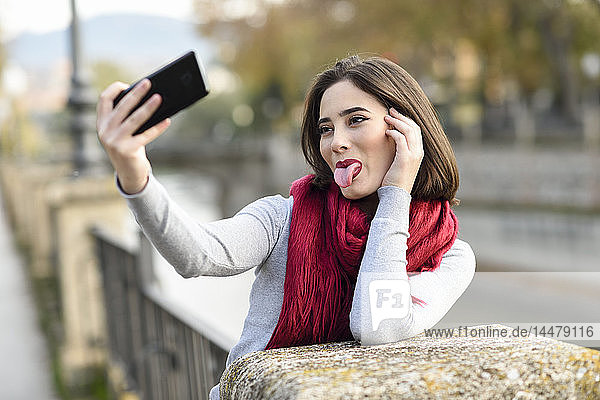 Porträt einer jungen Frau mit rotem Schal und herausgestreckter Zunge  die mit dem Handy Selbstgespräche führt