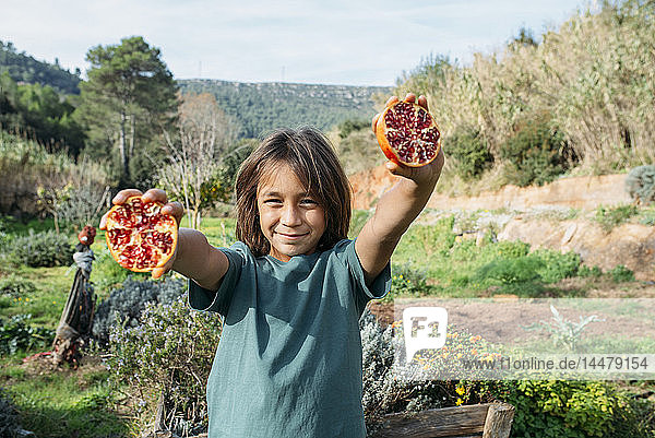 Junge hält halbierten Granatapfel in einem Obstgarten