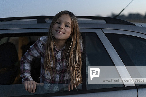 Porträt eines lächelnden Mädchens  das sich abends aus dem Autofenster lehnt