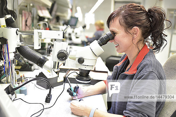 Woman using a microscope for the quality control in the manufacturing of circuit boards for the electronics industry