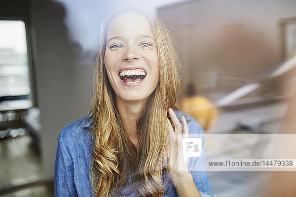 Porträt einer lachenden jungen Frau hinter einer Fensterscheibe