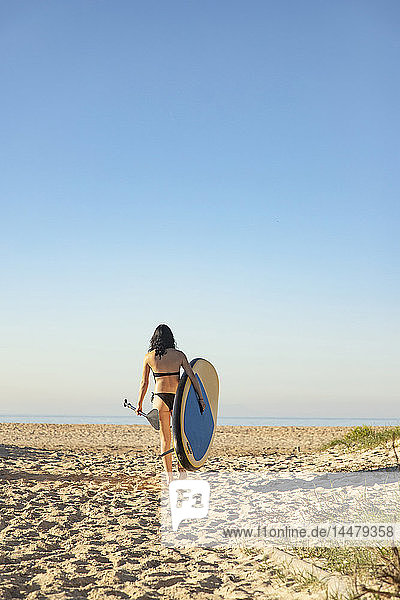 Spanien  Andalusien  Tarifa  Frau  die mit aufrechtem Paddelbrett am Strand spazieren geht