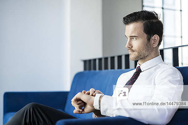 Businessman sitting on blue couch in office checking smartwatch