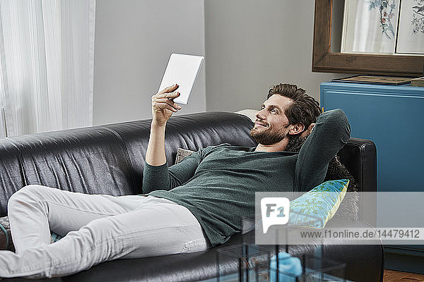 Smiling man with tablet lying on couch at home