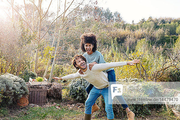 Man carrying girlfriend piggyback in a garden in the countryside