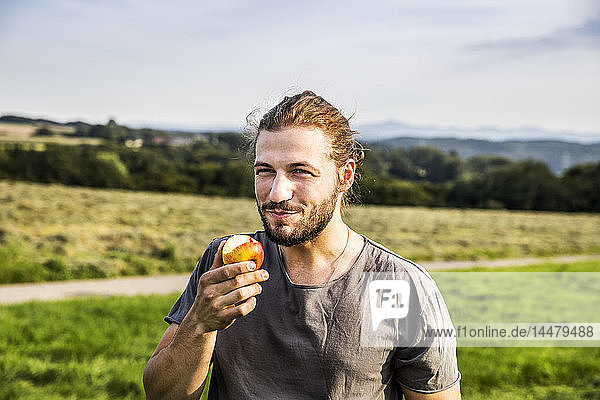 Junger Mann isst einen Apfel in ländlicher Landschaft