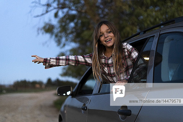 Porträt eines lächelnden Mädchens  das sich abends aus dem Autofenster lehnt