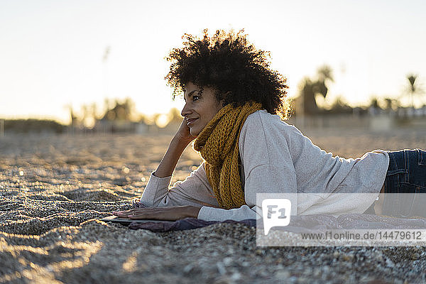 Frau  die im Sand liegt  sich am Strand entspannt und ein Buch liest