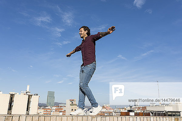 Mann auf einer Dachterrasse  der auf einer Mauer balanciert