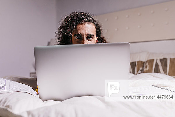 Portrait of young man in bed at home using laptop