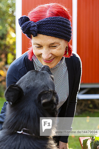 Porträt einer lächelnden älteren Frau mit rot gefärbtem Haar von Angesicht zu Angesicht mit ihrem Hund im Garten