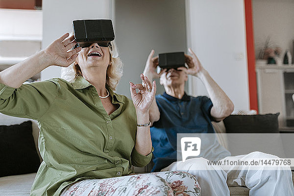 Glückliches älteres Ehepaar zu Hause  das mit einer VR-Brille auf der Couch sitzt