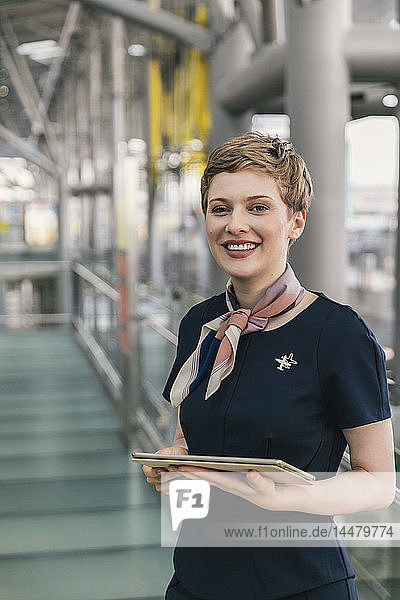 Porträt eines lächelnden Mitarbeiters einer Fluggesellschaft  der auf dem Flughafen eine Tablette in der Hand hält