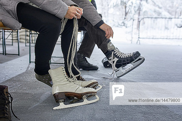 Paar  das auf einer Bank an der Eislaufbahn sitzt und Schlittschuhe anzieht