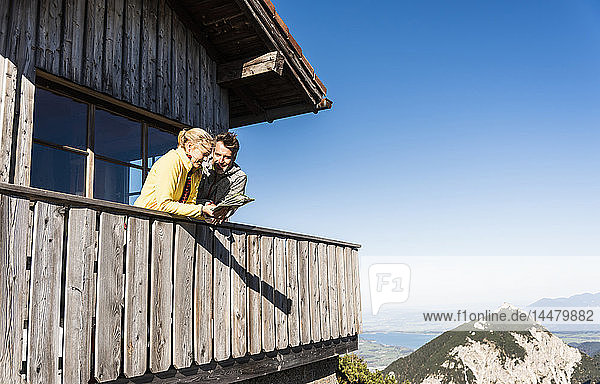 Paar lehnt auf dem Balkon einer Berghütte  hält Karte