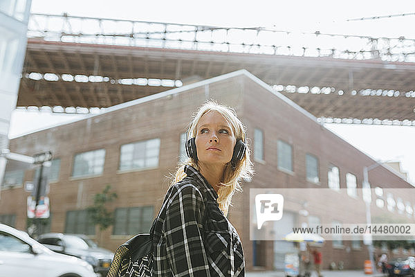 USA  New York City  Brooklyn  junge Frau  die in der Stadt mit Kopfhörern Musik hört und sich umsieht