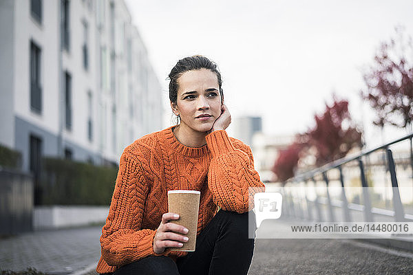 Portrait of pensive woman with coffee to go wearing orange knit pullover outdoors