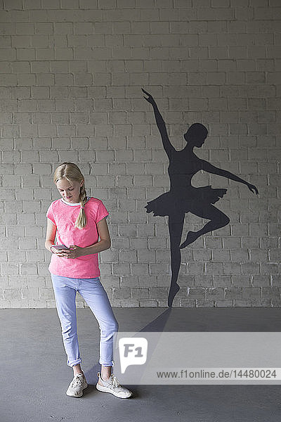 Blondes Mädchen mit Smartphone und Schatten einer Ballerina im Hintergrund