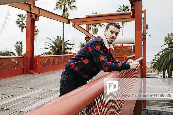 Junger Mann in legerer Kleidung auf einer roten Brücke mit Blick in die Kamera