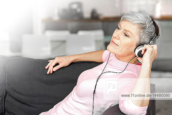 Porträt einer reifen Frau  die auf einer Couch sitzt und mit Kopfhörern Musik hört