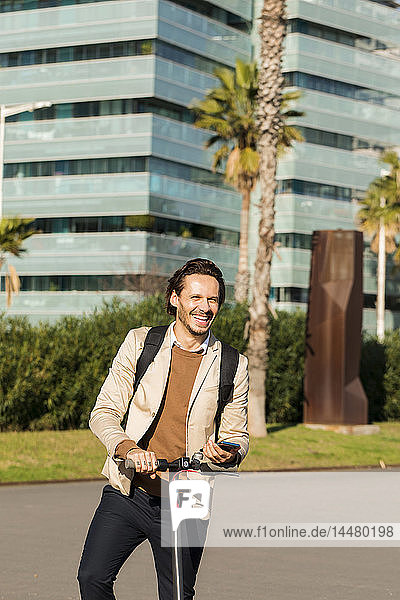 Porträt eines lachenden Mannes mit Rucksack und E-Scooter in der Stadt