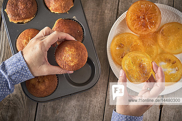 Frauenhände  die Muffins mit kandierten Orangenscheiben garnieren