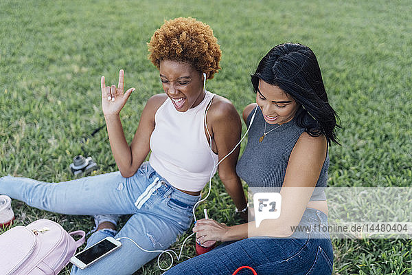 Two happy female friends relaxing in a park listening to music