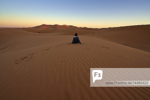 Marokko  Rückenansicht einer Frau  die in der Dämmerung auf einer Wüstendüne sitzt