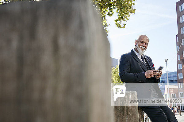 Elegant businessman leaning on wall in the city  using smartphone