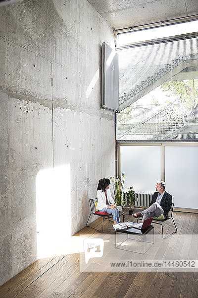 Businessman and businesswoman sitting in a loft at concrete wall talking