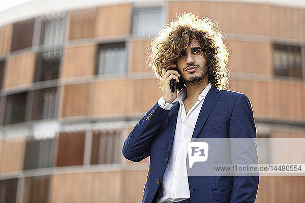 Portrait of young fashionable businessman with beard and curly hair on the phone