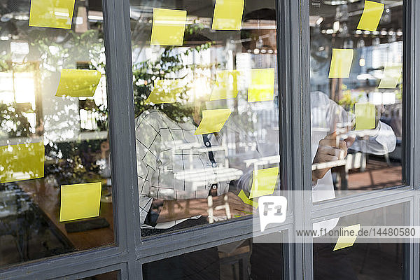 Businessman with colleague brainstorming with post-its on window front