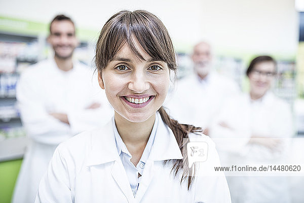 Portrait of smiling pharmacist in pharmacy with colleagues in background