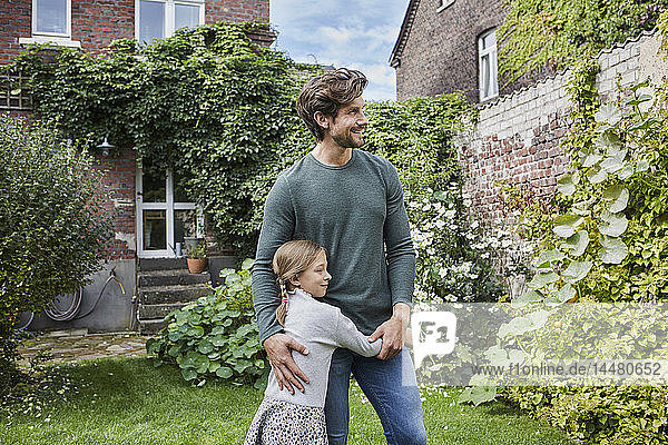 Lächelnder Vater mit Tochter steht im Garten ihres Hauses