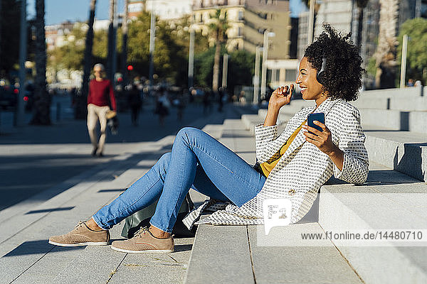 Schöne Frau sitzt auf einer Treppe in der Stadt  benutzt ein Smartphone  hört Musik mit Kopfhörern