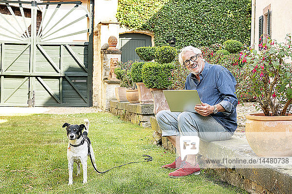 Porträt eines lachenden älteren Mannes mit Hund im Garten mit Tablette