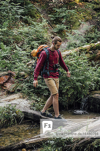 Young hiker with backpack crossing water in the forest