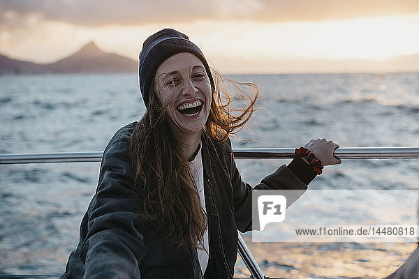 Südafrika  junge Frau mit Wollmütze lacht während einer Bootsfahrt bei Sonnenuntergang