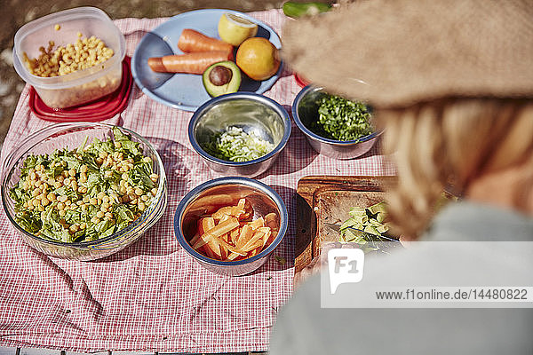 Frau bereitet vegetarisches Essen am Tisch im Freien zu
