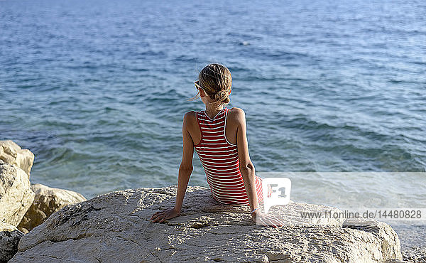 Kroatien  Lokva Rogoznica  Rückenansicht eines Mädchens  das auf einem Felsen vor dem Meer sitzt