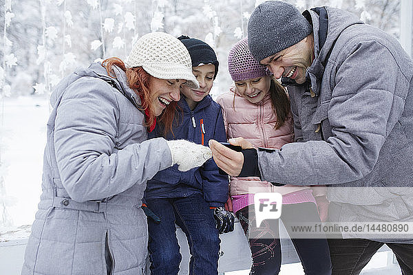 Family with two kids on the ice rink  looking at selfies on their smartphone