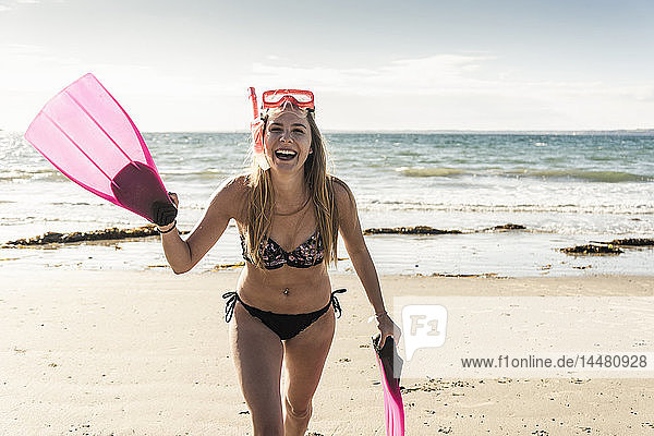 Glückliche junge Frau mit Schnorchelausrüstung  die am Strand läuft