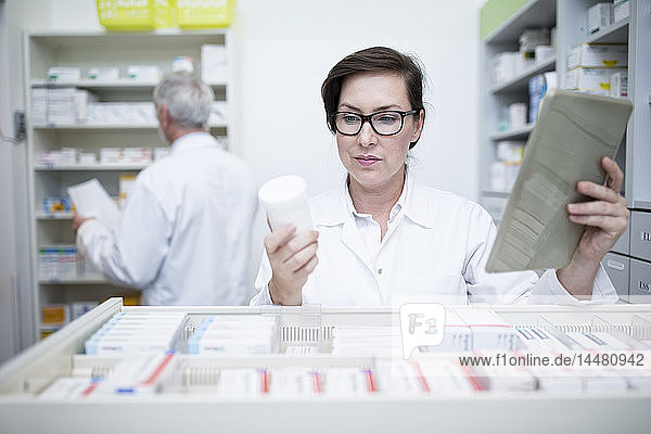 Pharmacist with tablet and medicine at cabinet in pharmacy