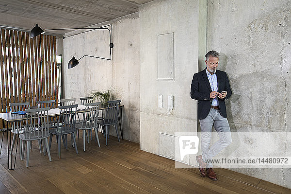 Businessman using cell phone leaning against concrete wall in a loft