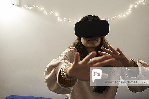 Junge Frau mit VR-Headsets spielt nachts zu Hause auf dem Sofa Spiele